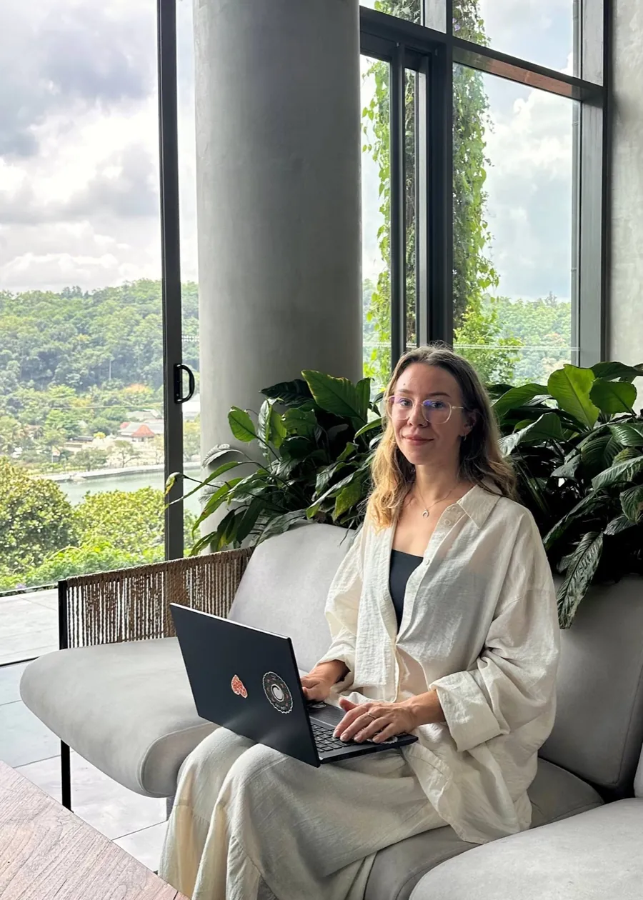 Tanya with her laptop in a bright room full of tropical plants