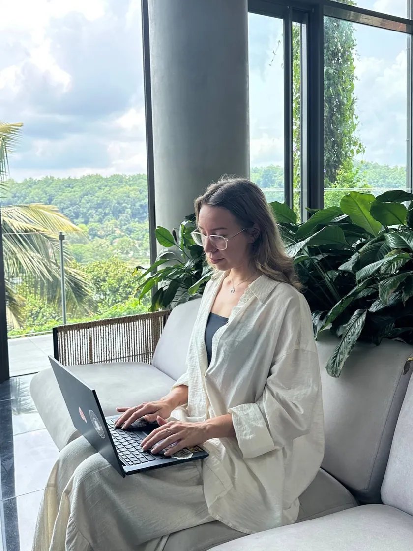 Tanya typing on her laptop by a big window